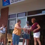 A group of people are shaking hands in front of a pepsi cola store.