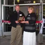 A man and a woman are standing in front of a building holding a plaque.