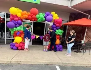 A group of people are standing in front of a building decorated with balloons.