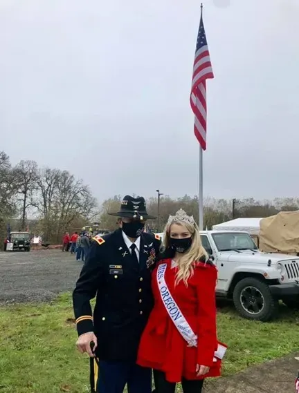 A man in a military uniform and a woman in a red dress are posing for a picture in front of an american flag.