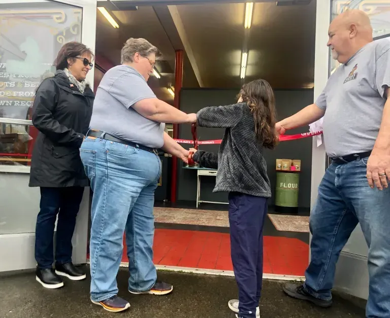 A group of people are standing in front of a store cutting a red ribbon