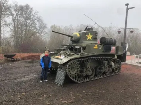 A young boy is standing in front of a military tank.