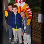 Three young boys are posing for a picture with mcdonald 's clown.