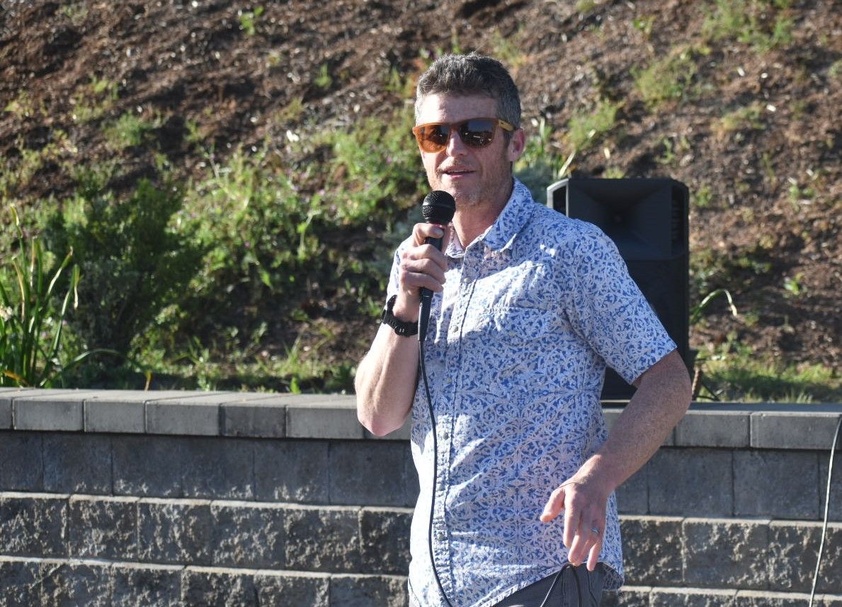 A man wearing sunglasses is holding a microphone in front of a speaker.