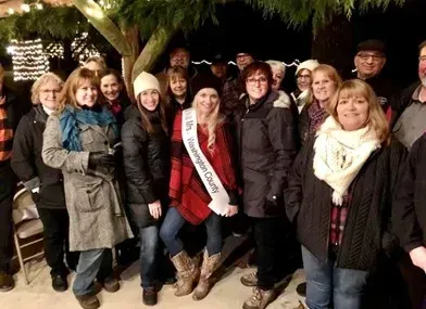 A group of people are posing for a picture with one woman wearing a sash that says ' christmas queen ' on it