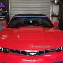 Red Chevrolet Camaro convertible parked in front of a garage door; car is in bright sunlight.