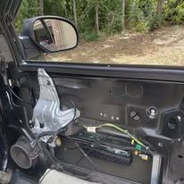 Interior view of a car door, disassembled. Wires, metal components, and the door mirror are visible.