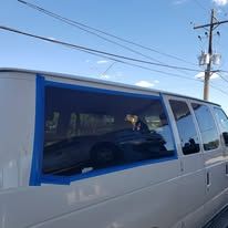 A white van with a large window covered in blue tape; a vehicle is visible inside the window.