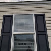 Window with white frame and dark blue shutters on a light-colored siding. The window has horizontal blinds.