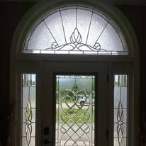 A decorative glass front door with sidelights. The door features an arched window with an ornate floral design, surrounded by clear glass.