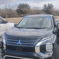 Black Mitsubishi SUV with a blue tape on the windshield parked outside.
