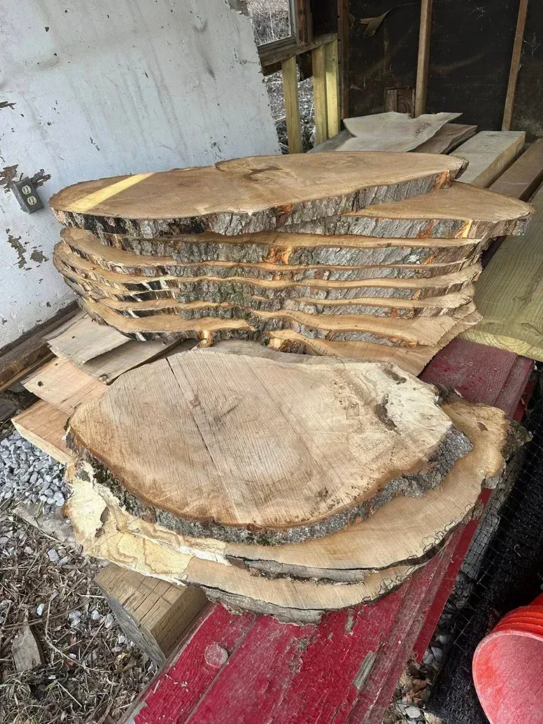 A stack of rustic, live-edge wood slices resting on a weathered red surface outdoors.