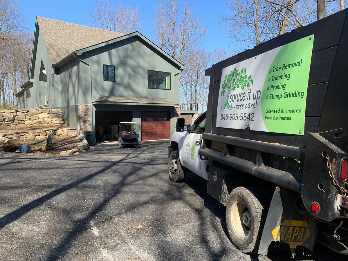 A work truck parked in the gravel driveway of a gray two-story house with a garage.