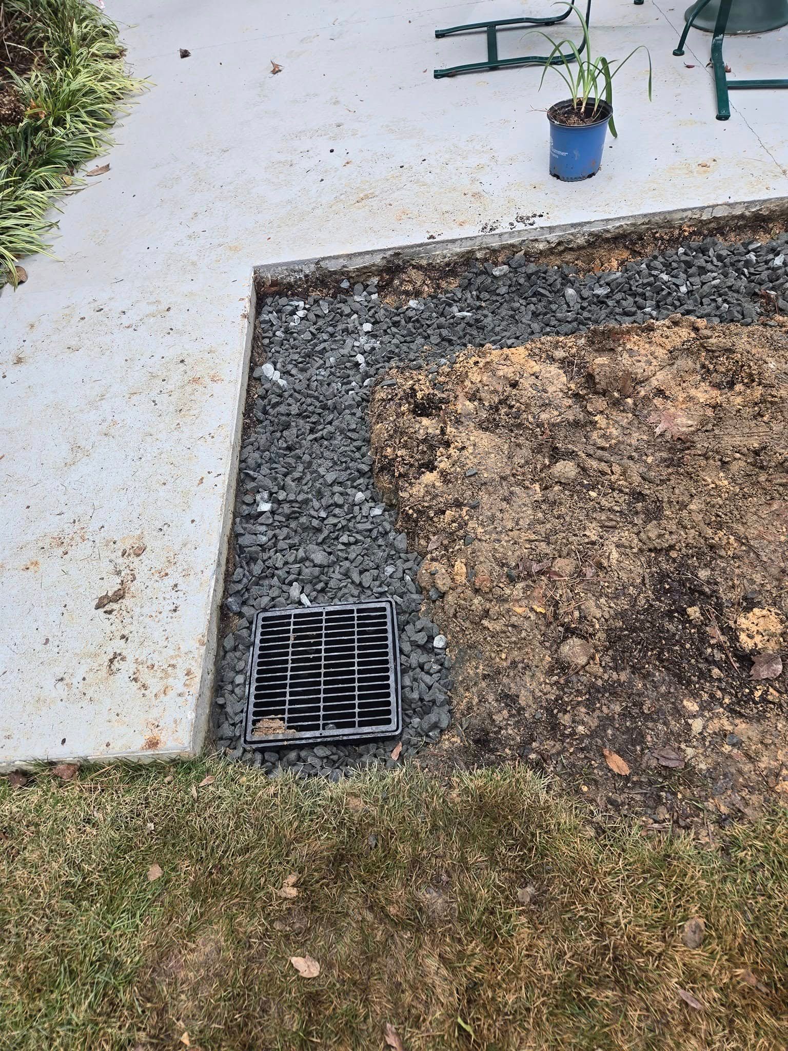 A drain is sitting in the middle of a yard next to a sidewalk.