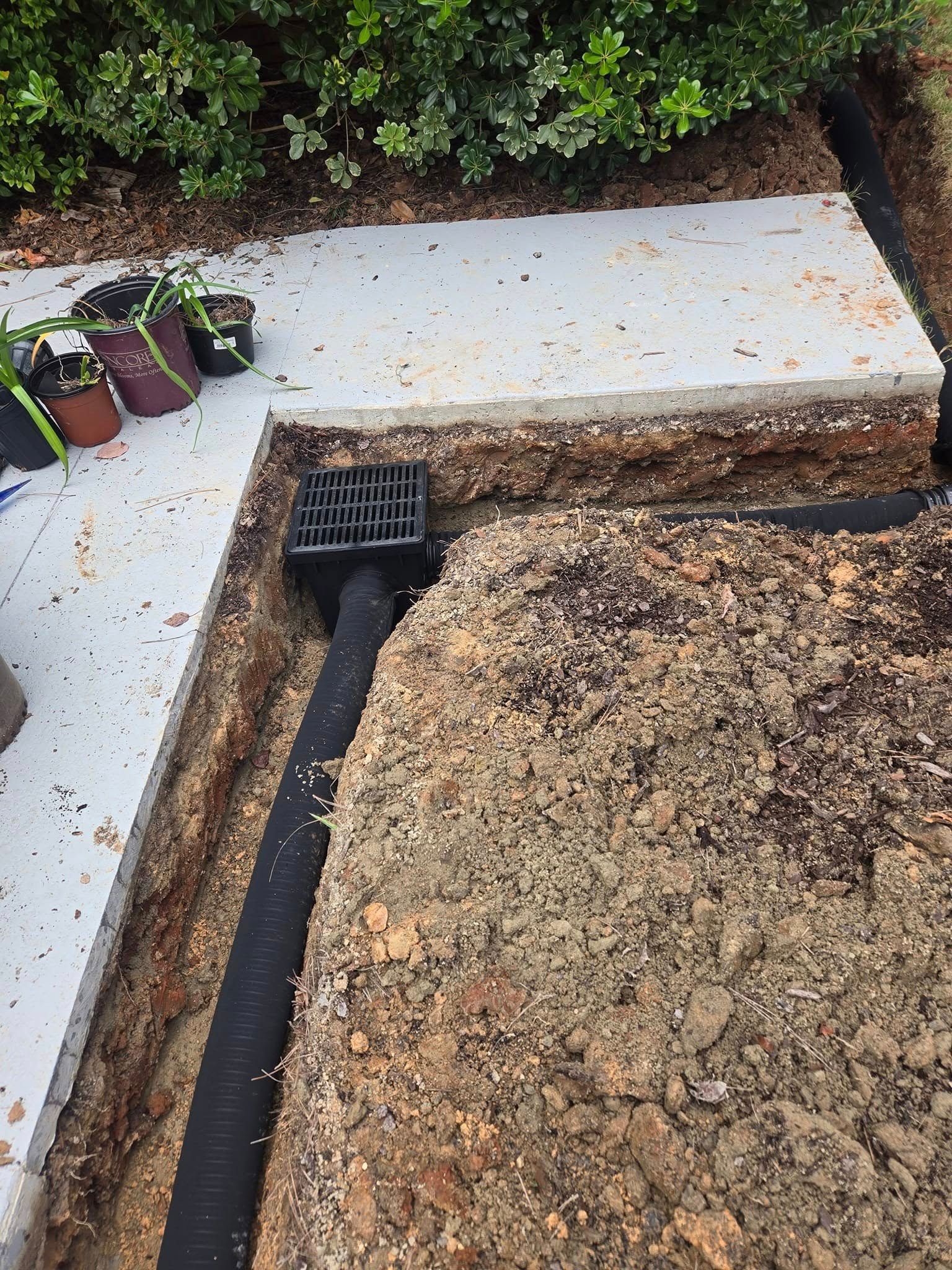 A black pipe is laying in the dirt next to a sidewalk.