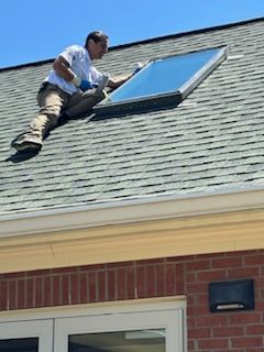 A man is sitting on top of a roof installing a skylight.