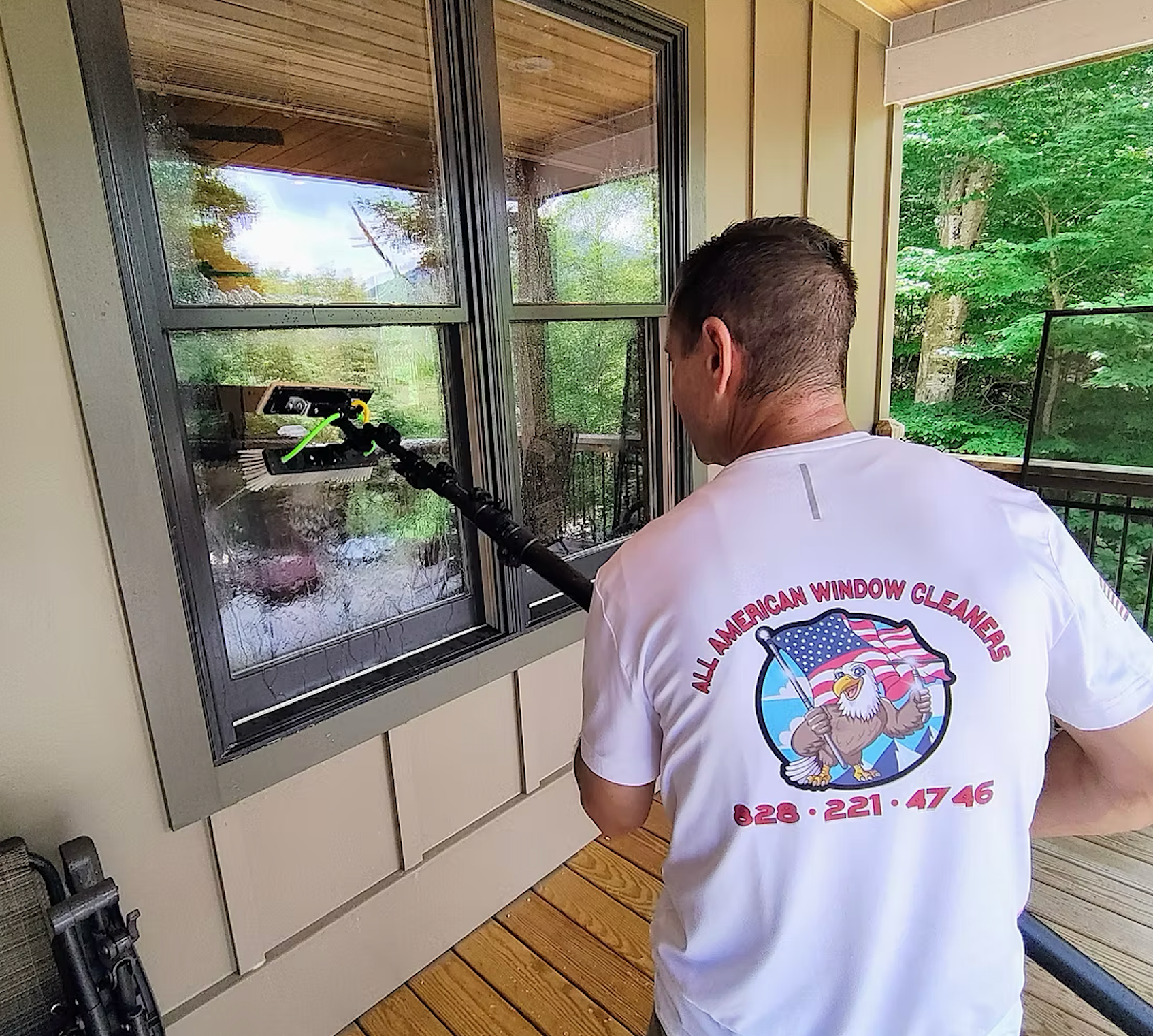 A man is cleaning a window with a vacuum on a porch.