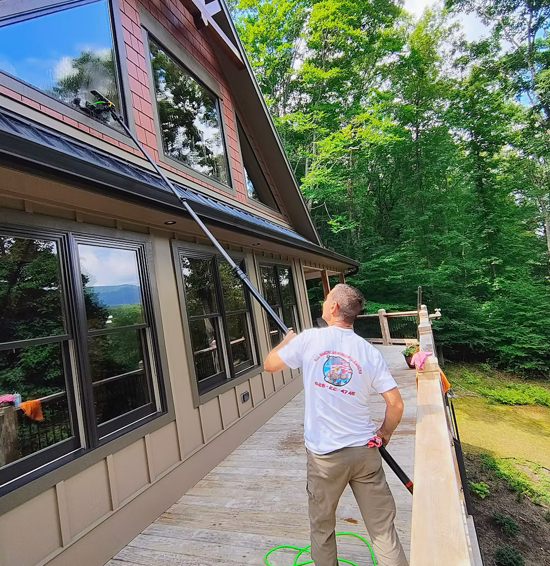 A man is cleaning the windows of a house with a hose.