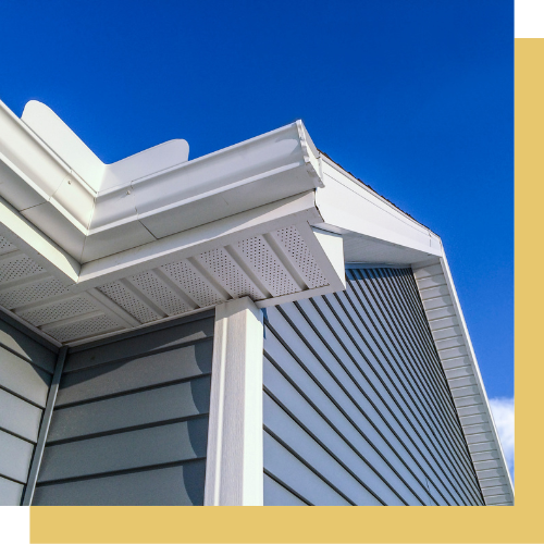 The corner of a house with a white gutter and a blue sky in the background.