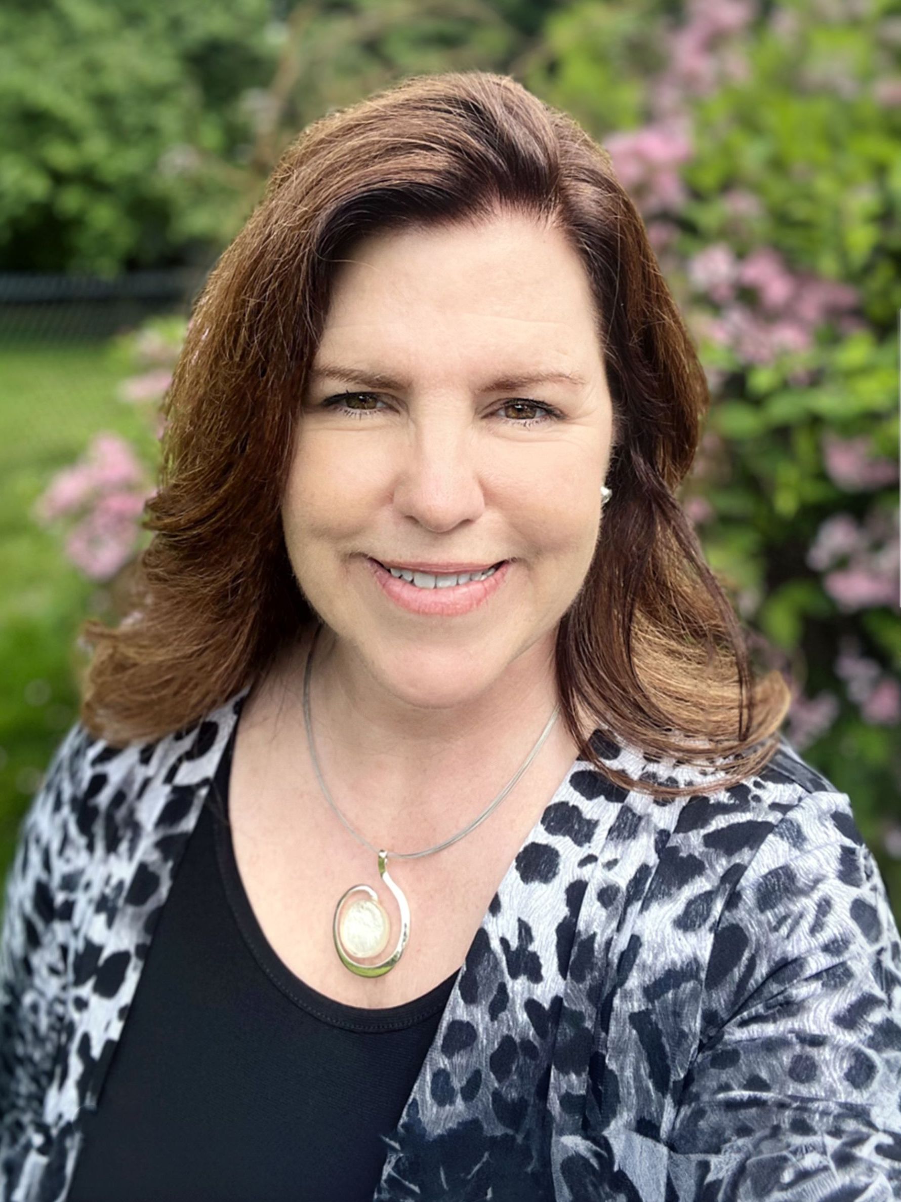 A woman wearing a necklace and a leopard print jacket is smiling for the camera.