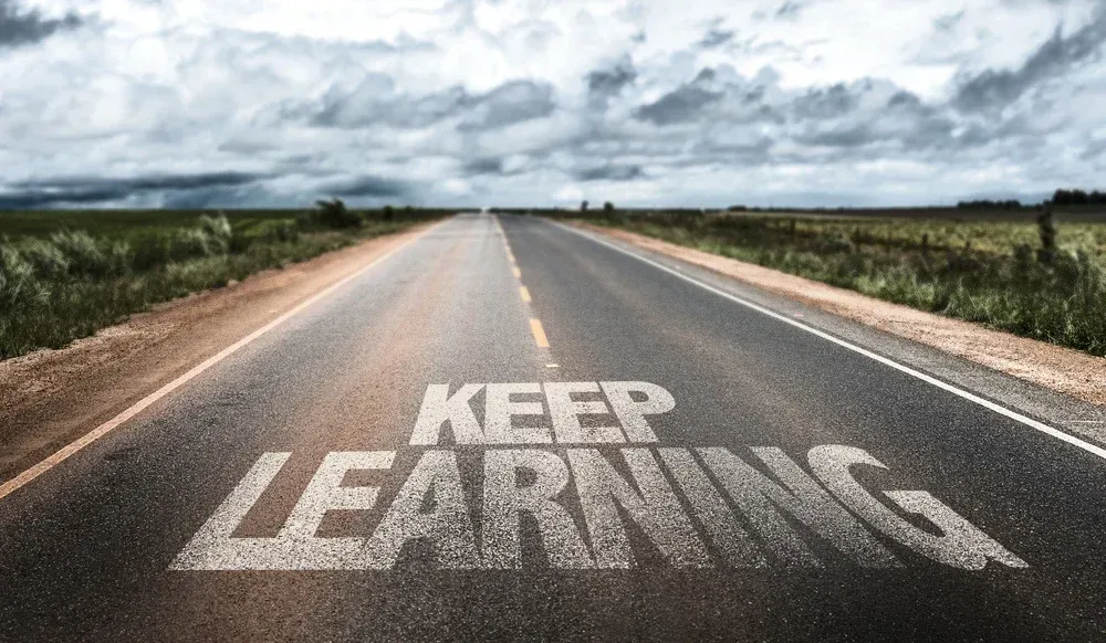 A highway road leading  into the distance with  fluffy clouds with the words Keep Learning on it.