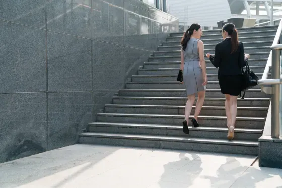 2 business dressed women walking up outdoor stairs having a conversation