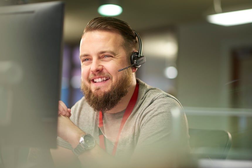 A man with a beard is wearing a headset while sitting in front of a computer.