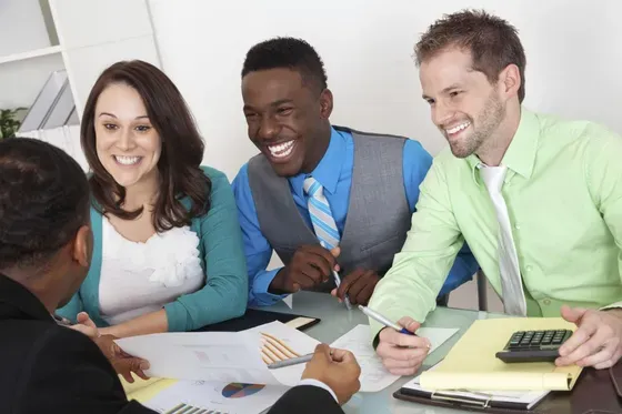 Young men and women in an office setting collaborating around a table smiling at each other.