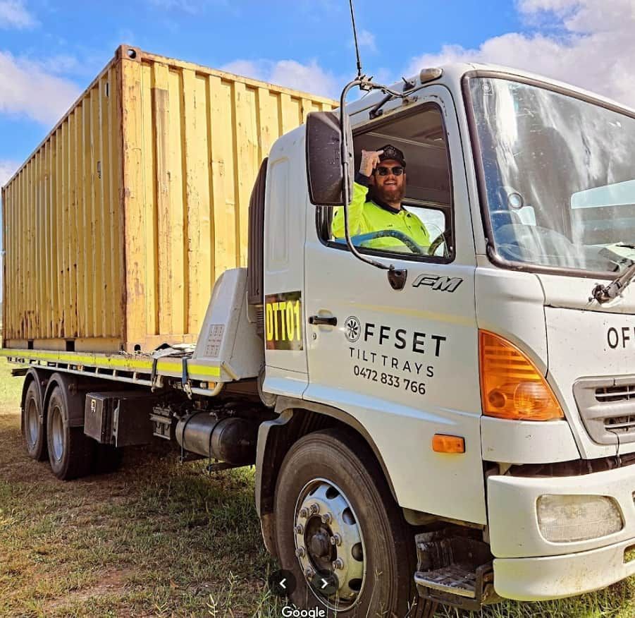 A Man Is Driving a Truck with A Yellow Container on The Back — Offset Tilt Trays In Biloela, QLD
