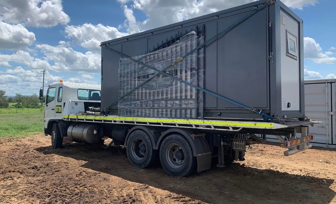 A Semi Truck With A Gray Container On The Back Is Driving Down A Road — Offset Tilt Trays In Biloela, QLD