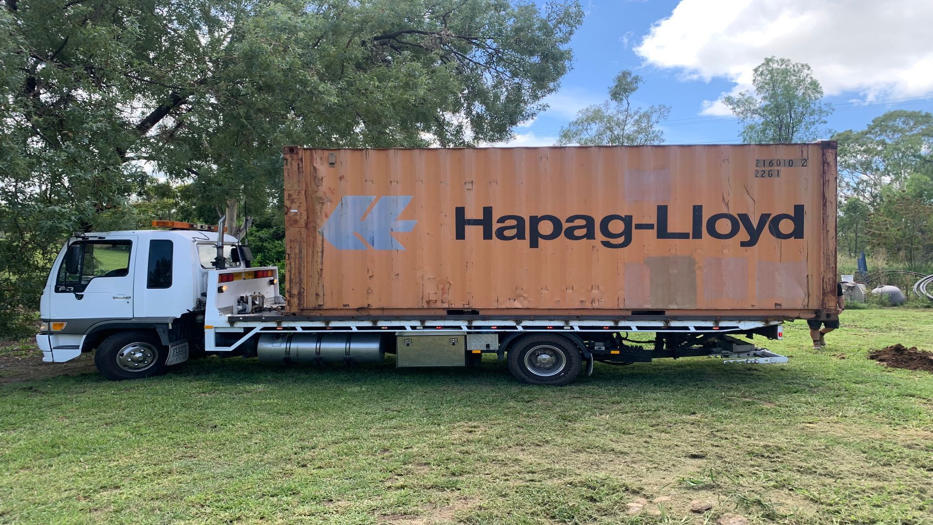 A Semi Truck With A Gray Container On The Back Is Driving Down A Road — Offset Tilt Trays In Biloela, QLD