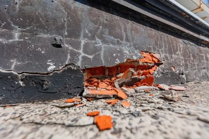 Close-up of crumbling exterior foundation wall showing severe concrete deterioration and exposed red brick.