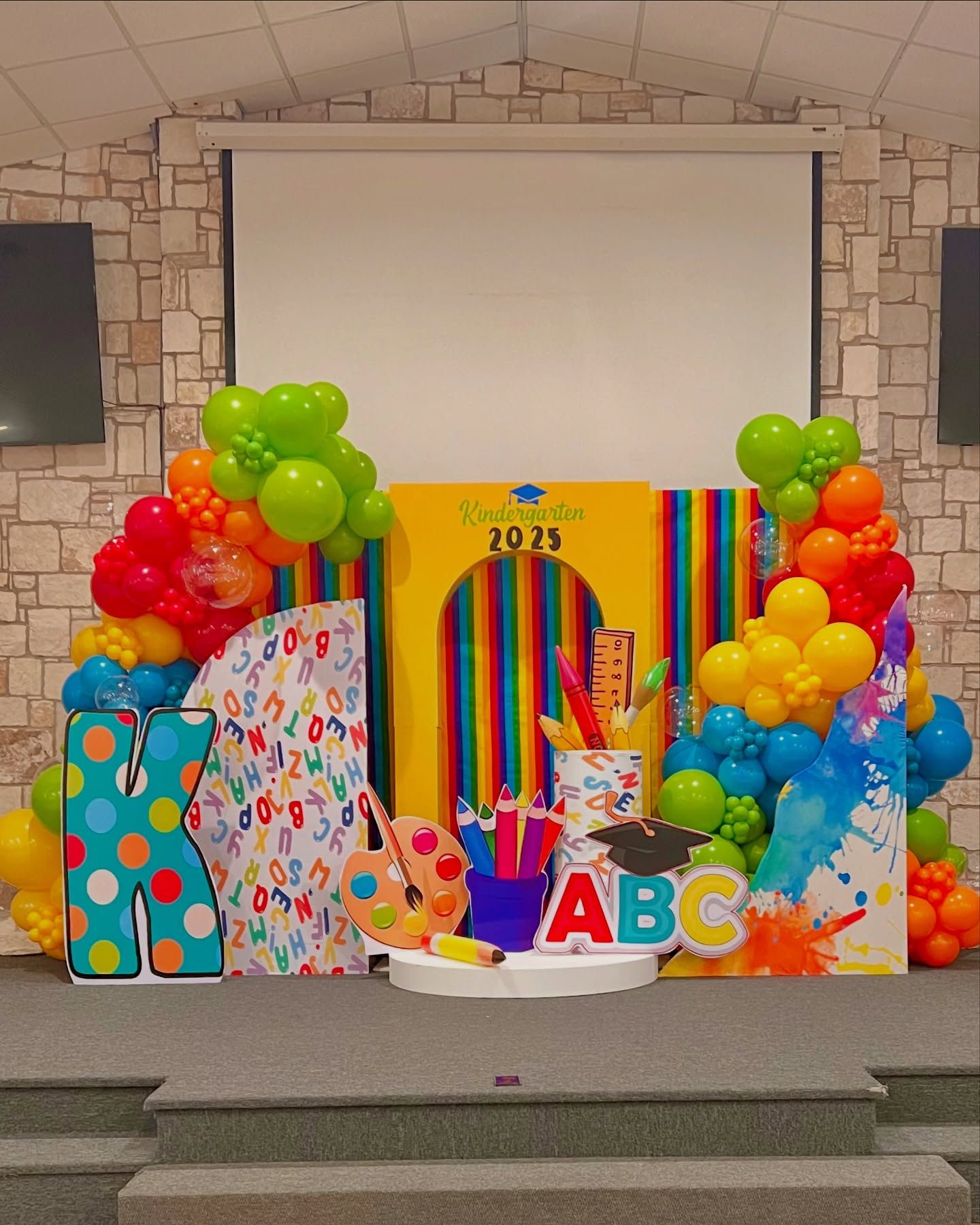 A stage decorated with balloons , letters , and numbers for a graduation party.