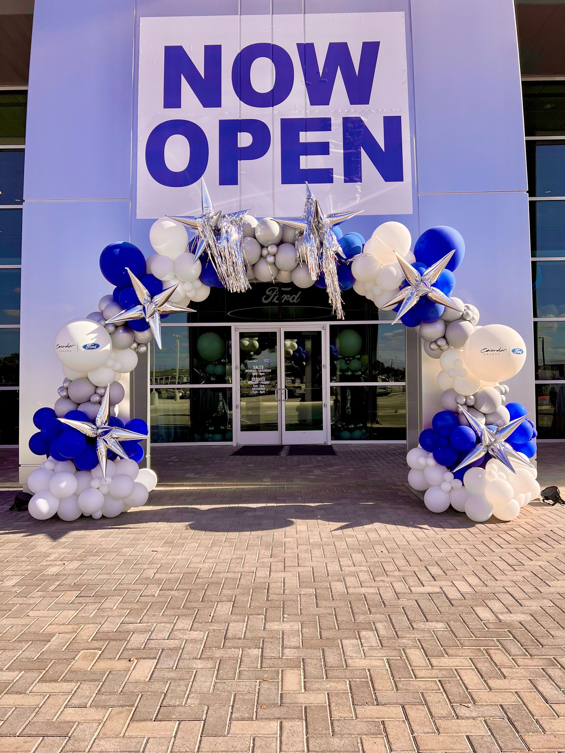A store front with balloons and a sign that says `` now open ''.