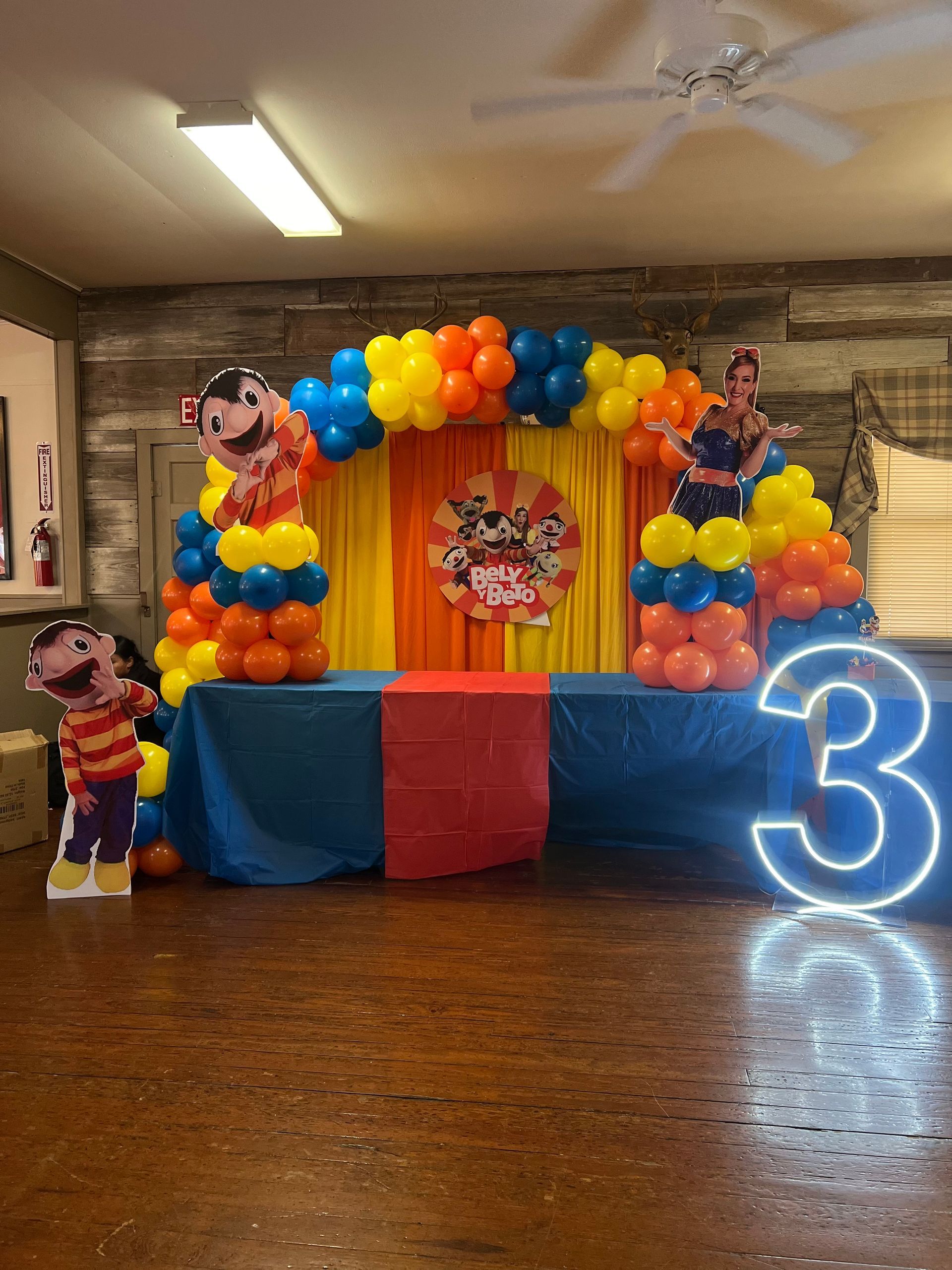 A room decorated with balloons and a table with a neon number 3.