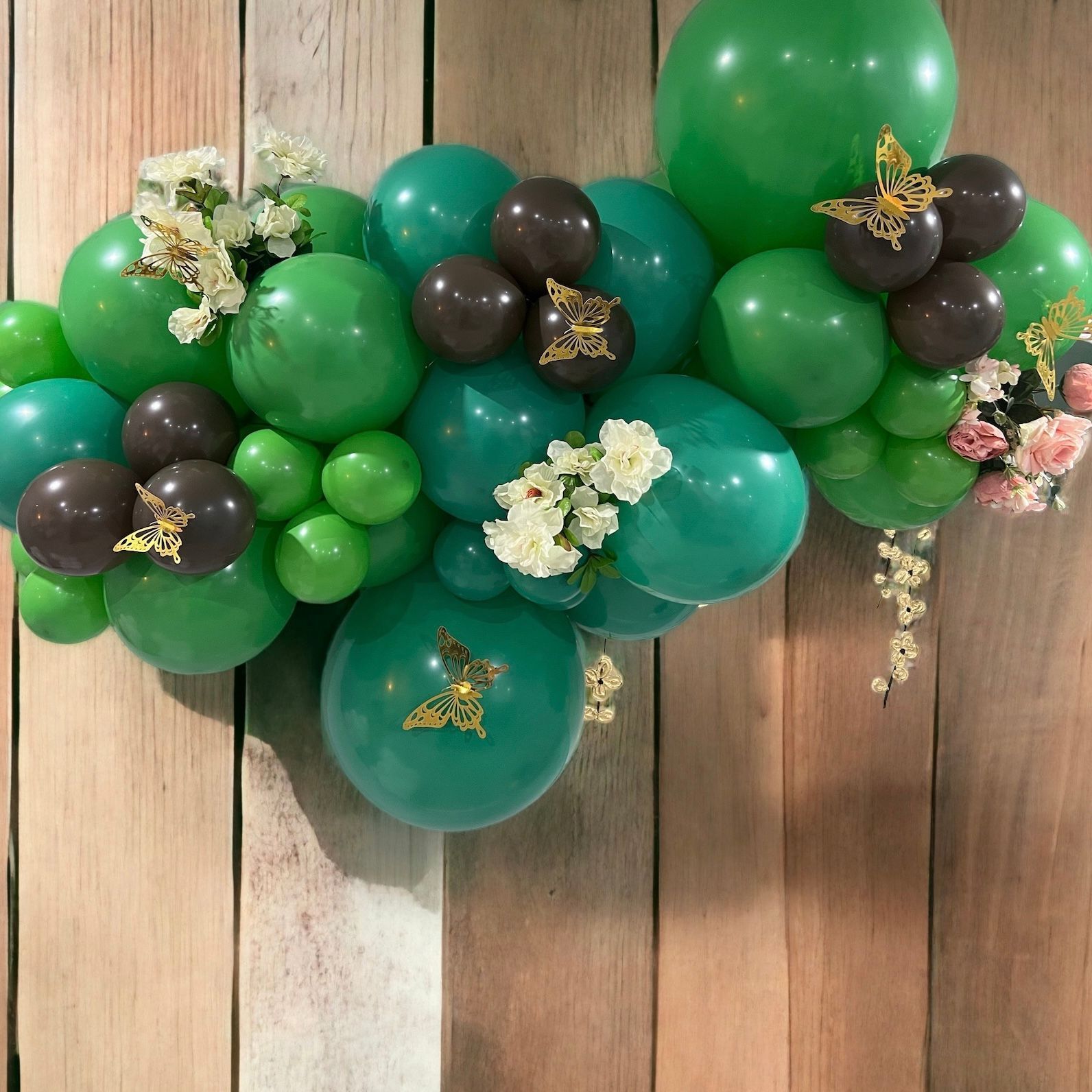 A bunch of green balloons and flowers on a wooden wall