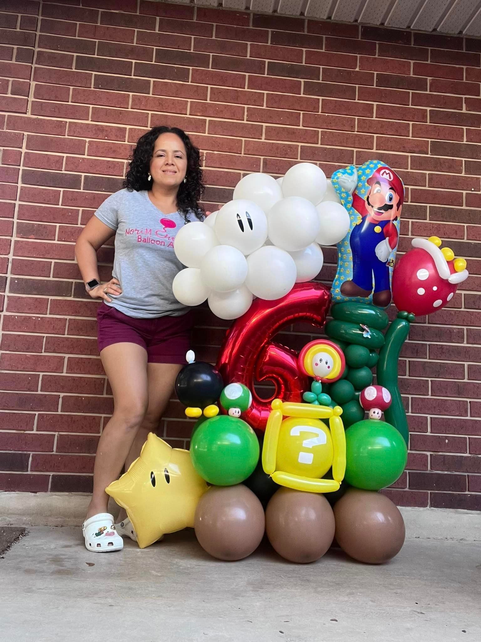 A woman is standing next to a bunch of balloons in front of a brick wall.