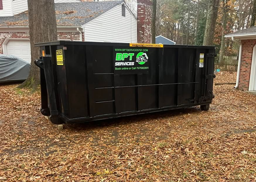 Black dumpster in a yard with fall leaves. Green logo reads 
