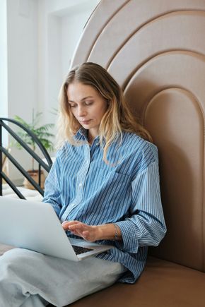 A woman is sitting on a couch using a laptop computer.