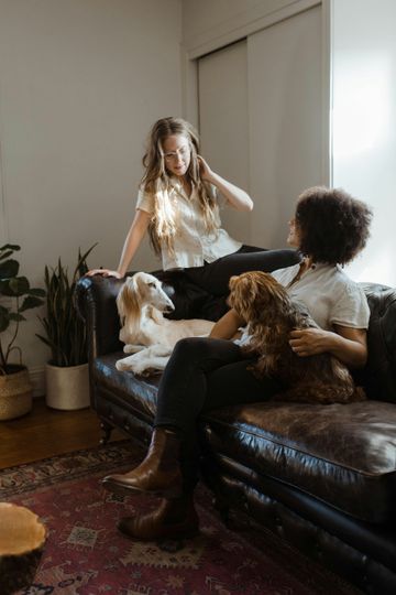 Two women are sitting on a couch with their dogs.