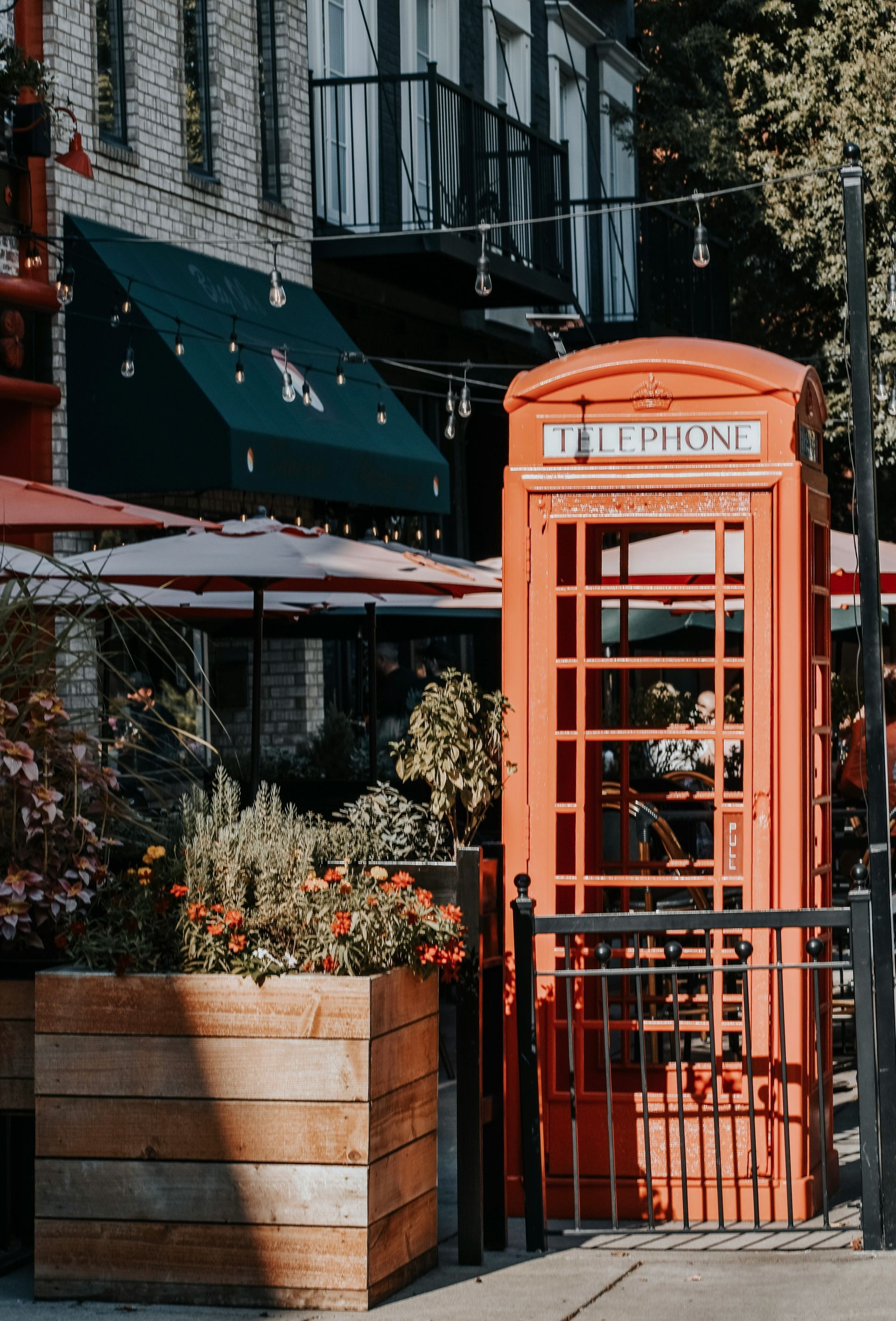 A red telephone booth is sitting on the sidewalk in front of a restaurant.