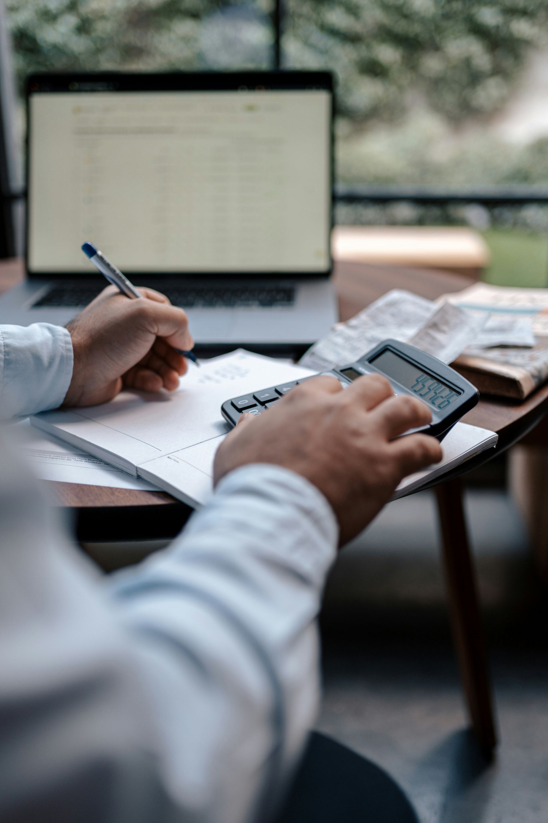 A man is sitting at a desk using a calculator and writing on a piece of paper.