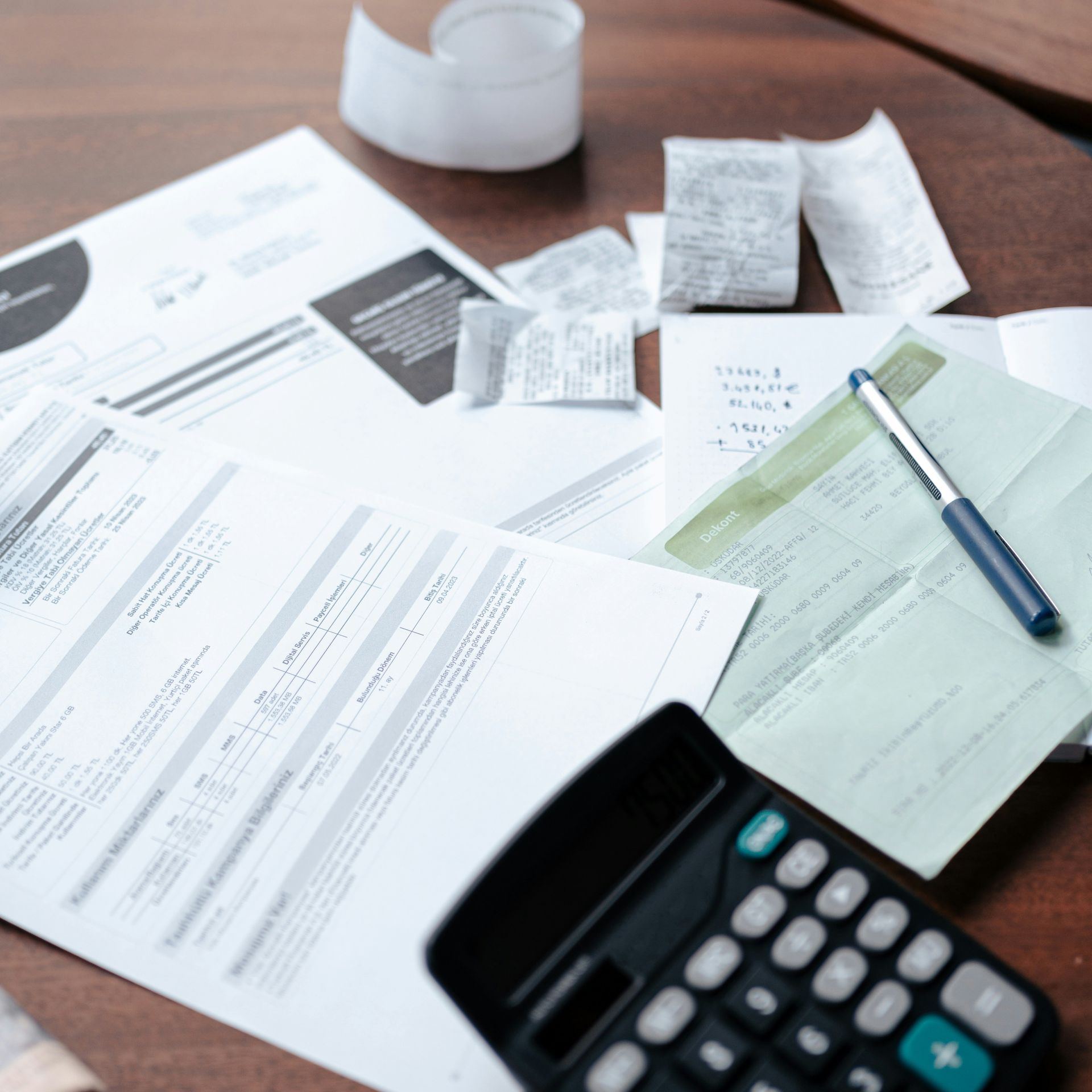 A calculator sits on a table surrounded by papers and receipts