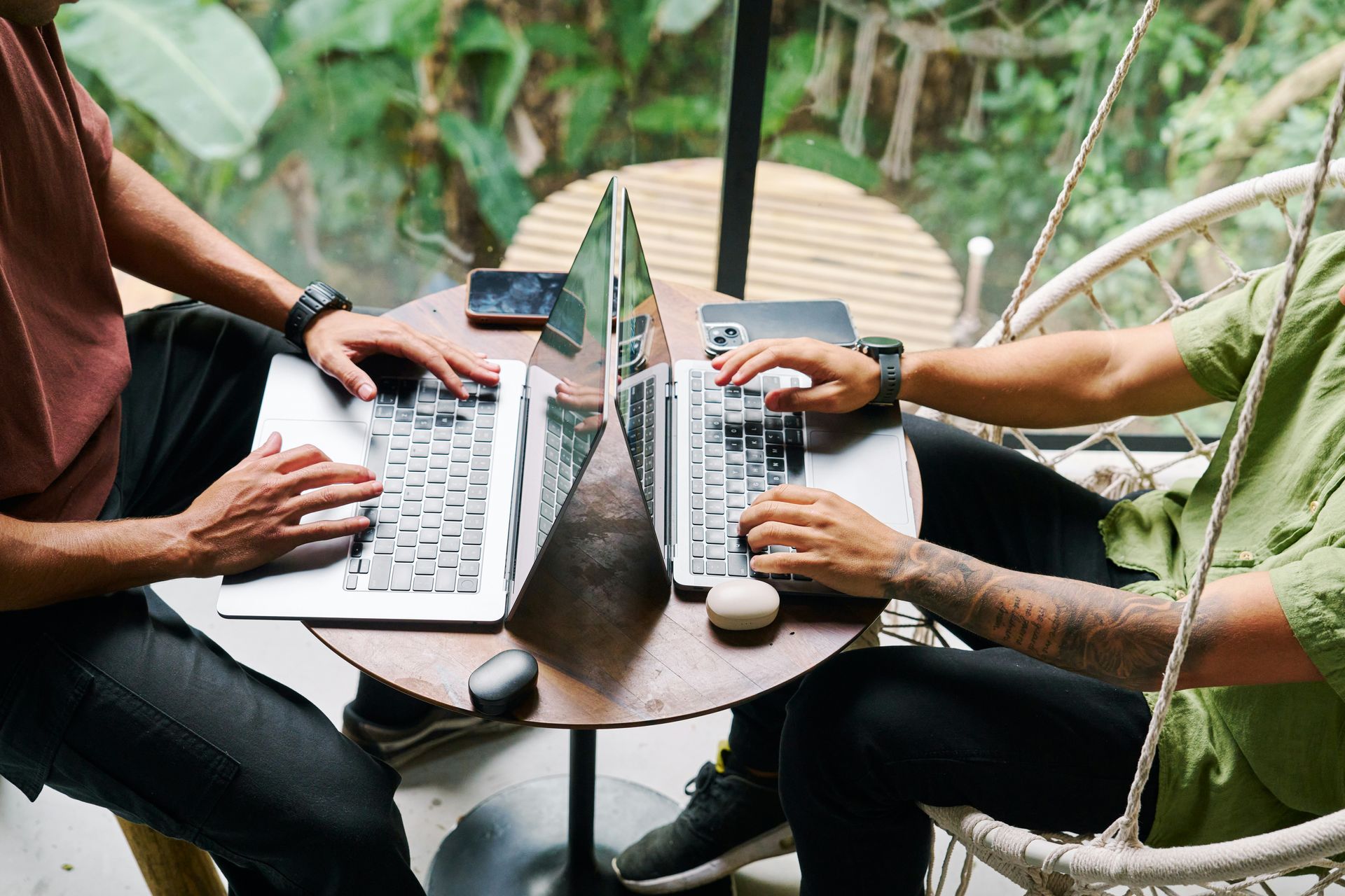 Two men are sitting at a table using laptops.