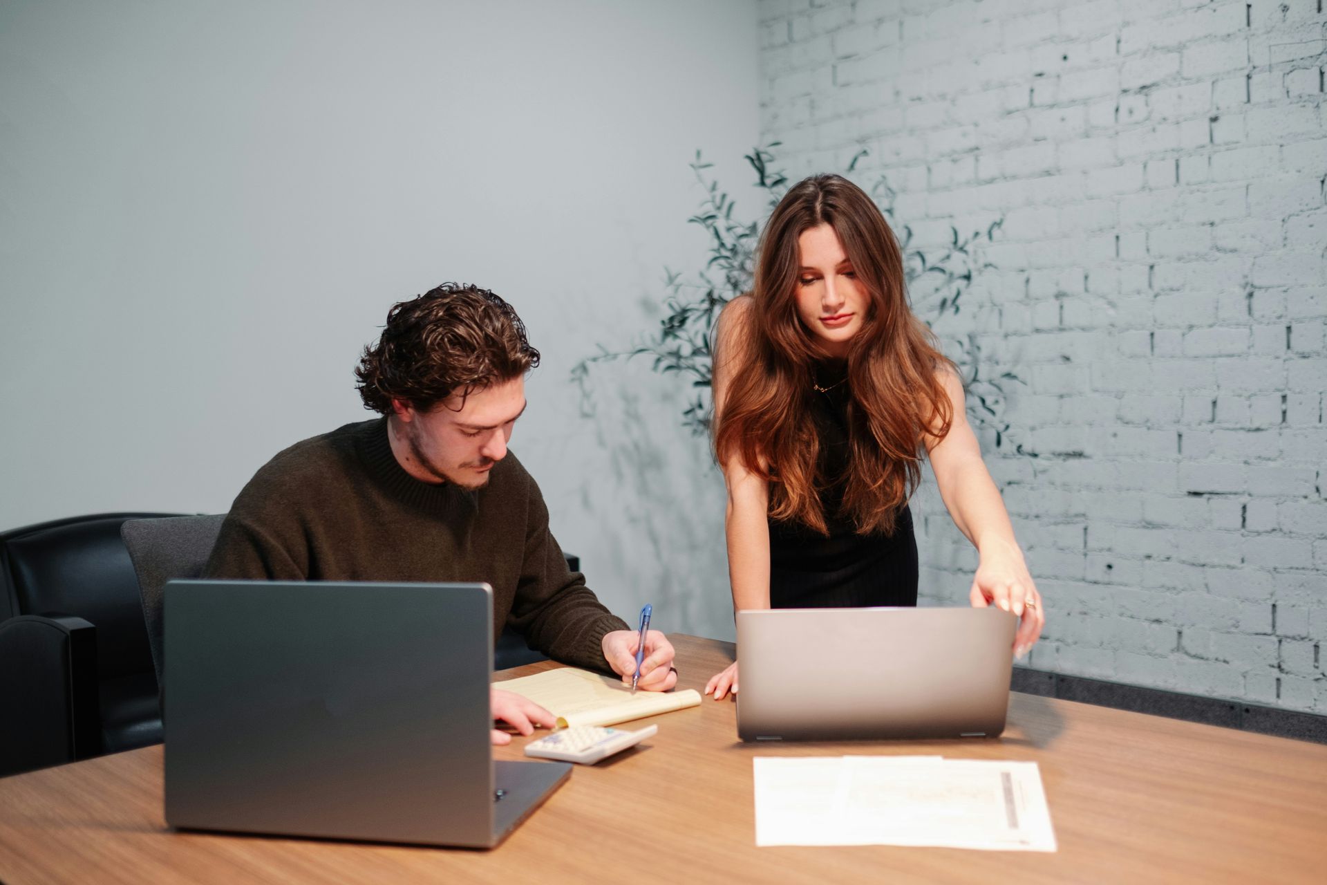 A man and a woman are sitting at a table with laptops.