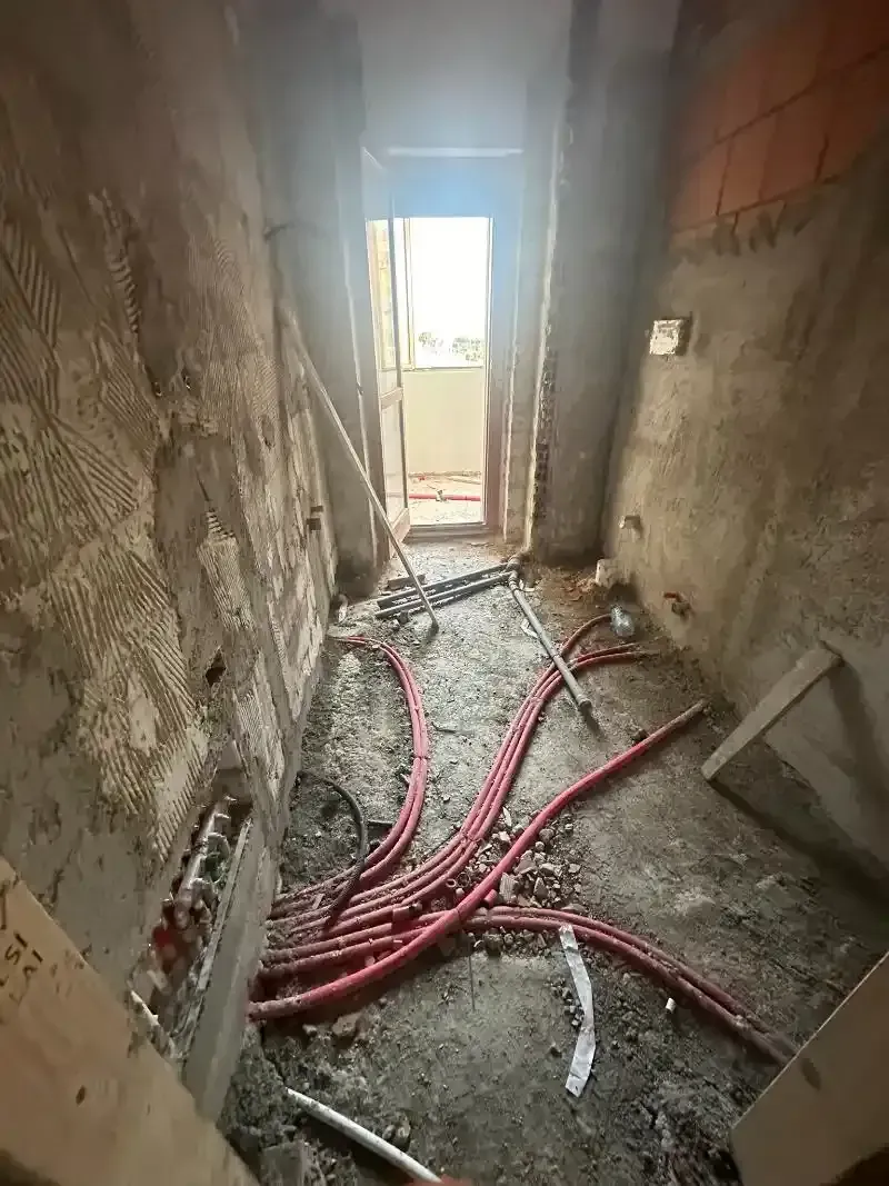 Corridoio interno in costruzione; tubi rossi sul pavimento, porta in fondo, pareti grezze.