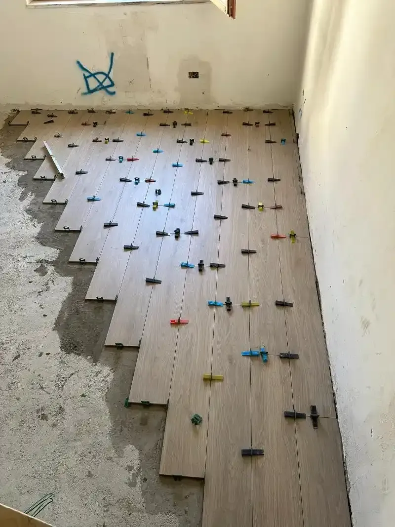 Piastrelle effetto legno installate su un pavimento in cemento mediante clip di livellamento, in una stanza con una parete chiara.