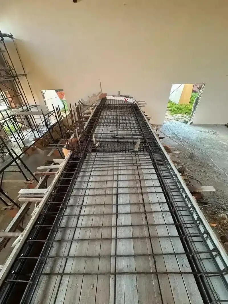 Vista del cantiere: struttura di fondazione in cemento armato pronta per il getto; casseforme e barre di armatura.