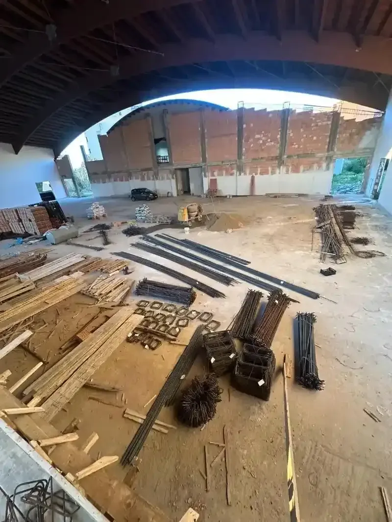 Interno di un edificio in costruzione, con travi sparse in legno e metallo. Pareti in mattoni a vista e soffitto a volta.