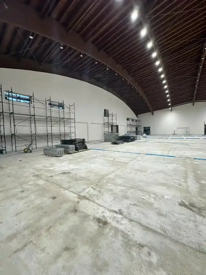 Ampio spazio interno vuoto in costruzione. Impalcature, pavimento in cemento, soffitto curvo, alcuni materiali presenti.